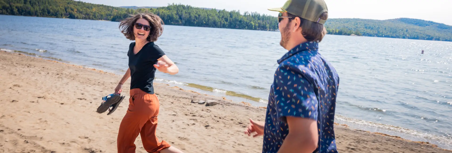A man and woman run on a beach at a lake.