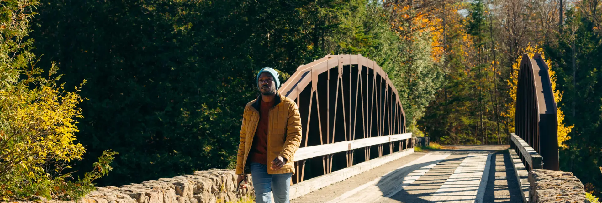 A man walks across a bridge in fall. 