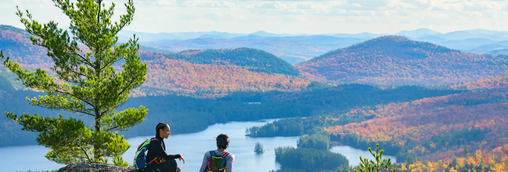 A man and woman sit on top of a mountain in fall. 