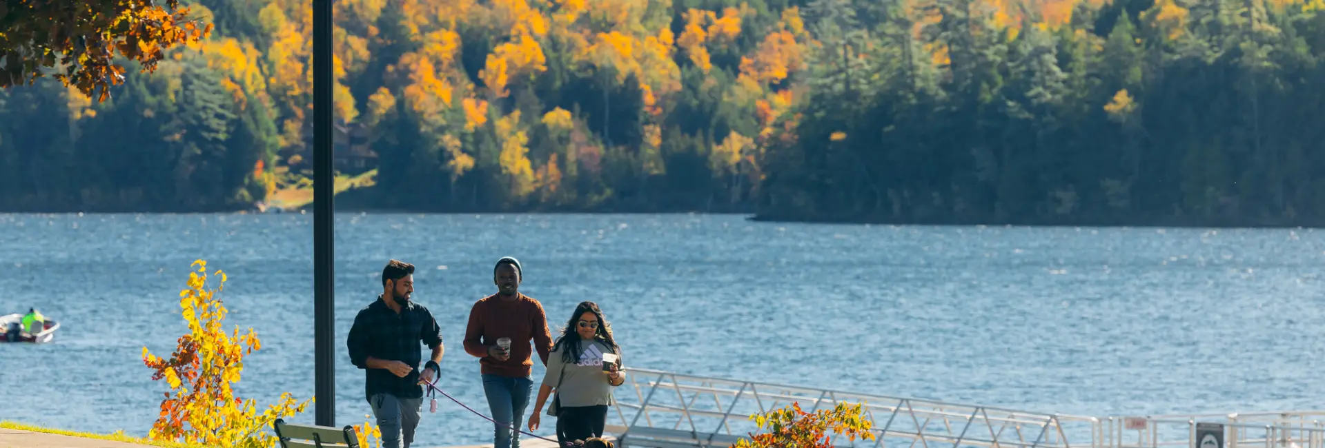 Three friends walk a trail along a lakefront in fall. 