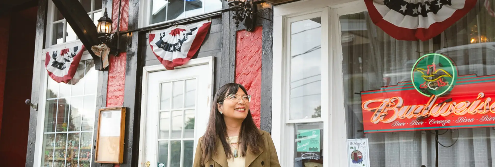 A woman wearing glasses smiles in front of a pub.