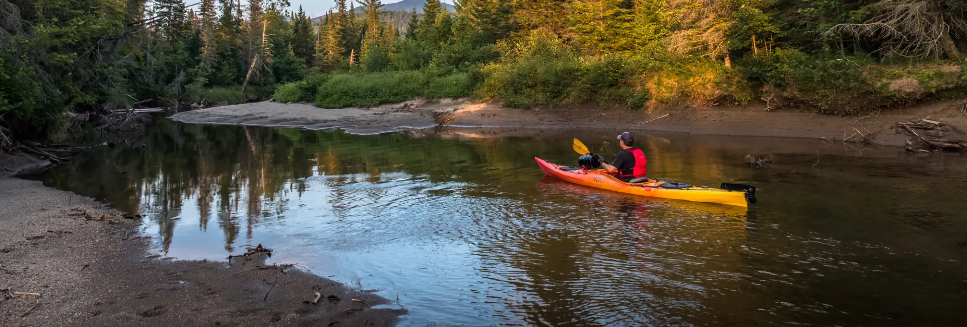 A man paddles in a kayak down a winding river. 