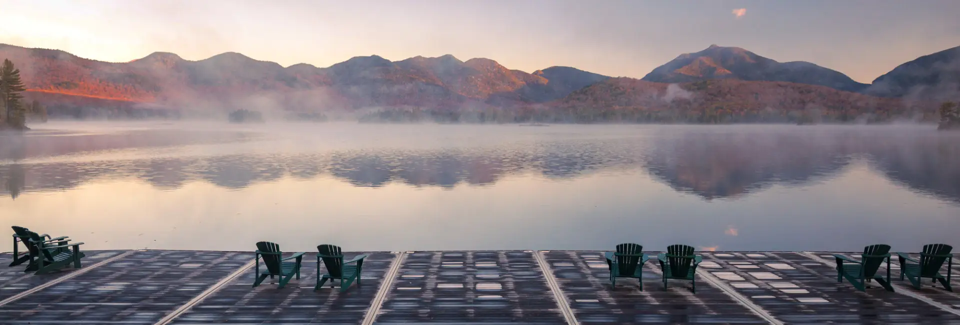 A luxurious dock on a still lake with mountains in the background.