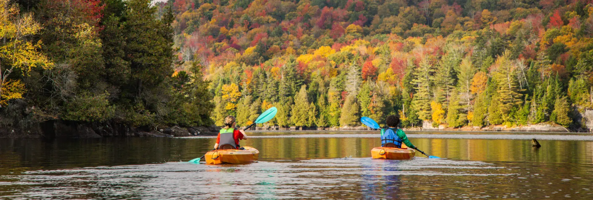 Two people paddle on a lake in fall.
