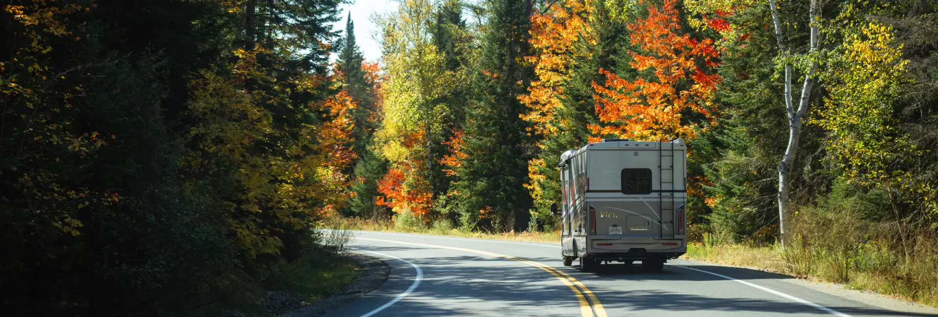 An RV drives on a winding road in fall. 