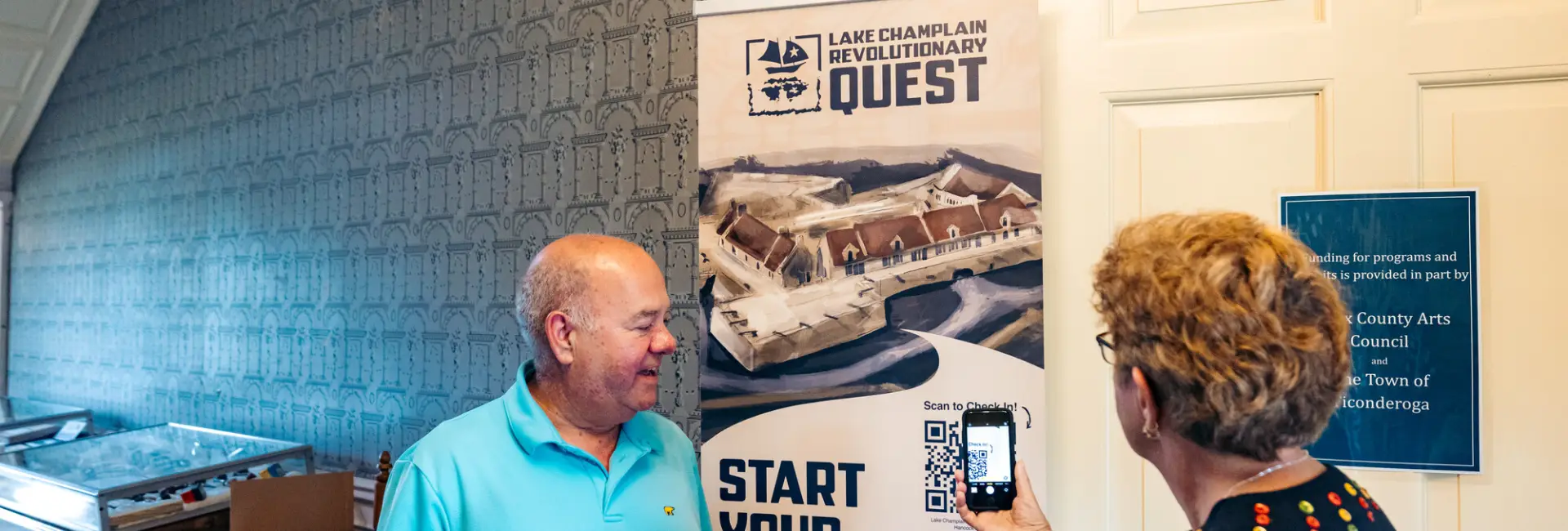 An old couple next to a banner for the Lake Champlain Revolutionary Quest