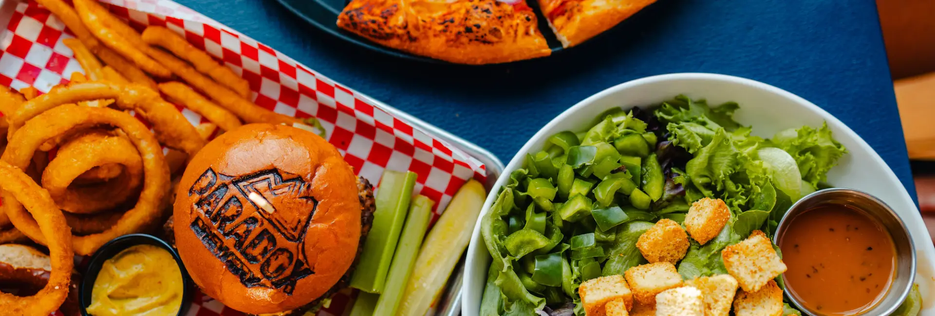 A spread of burgers, wings, pizza, and salad. 