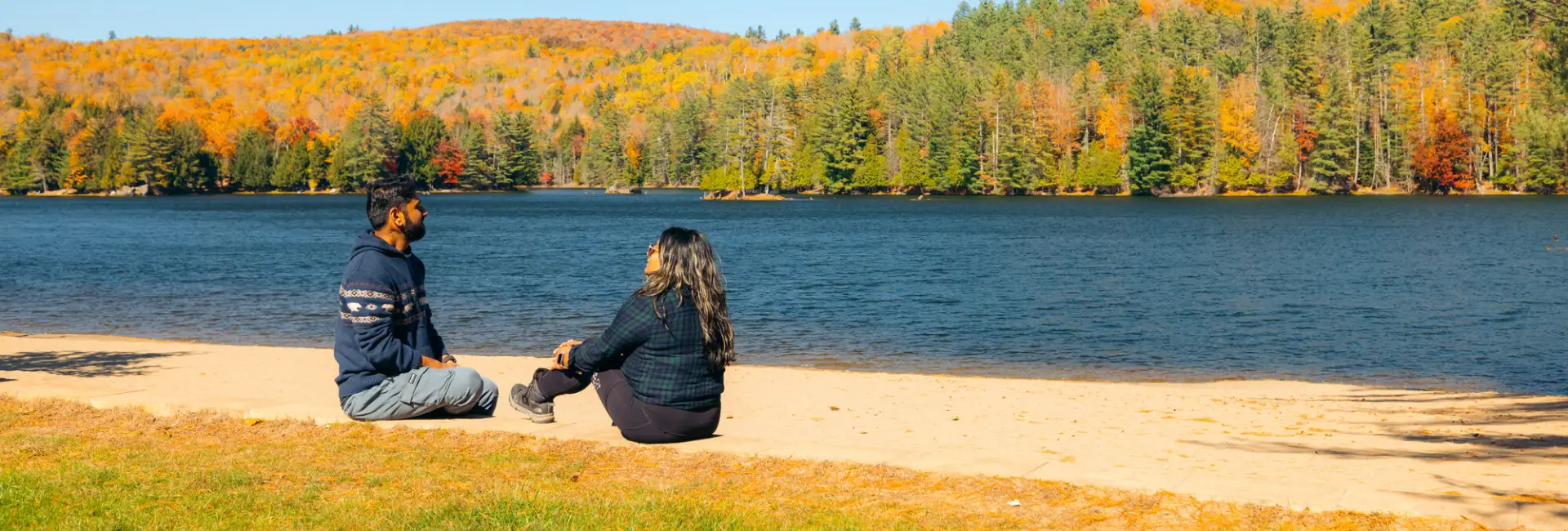 A man and woman sit on a fall beach. 