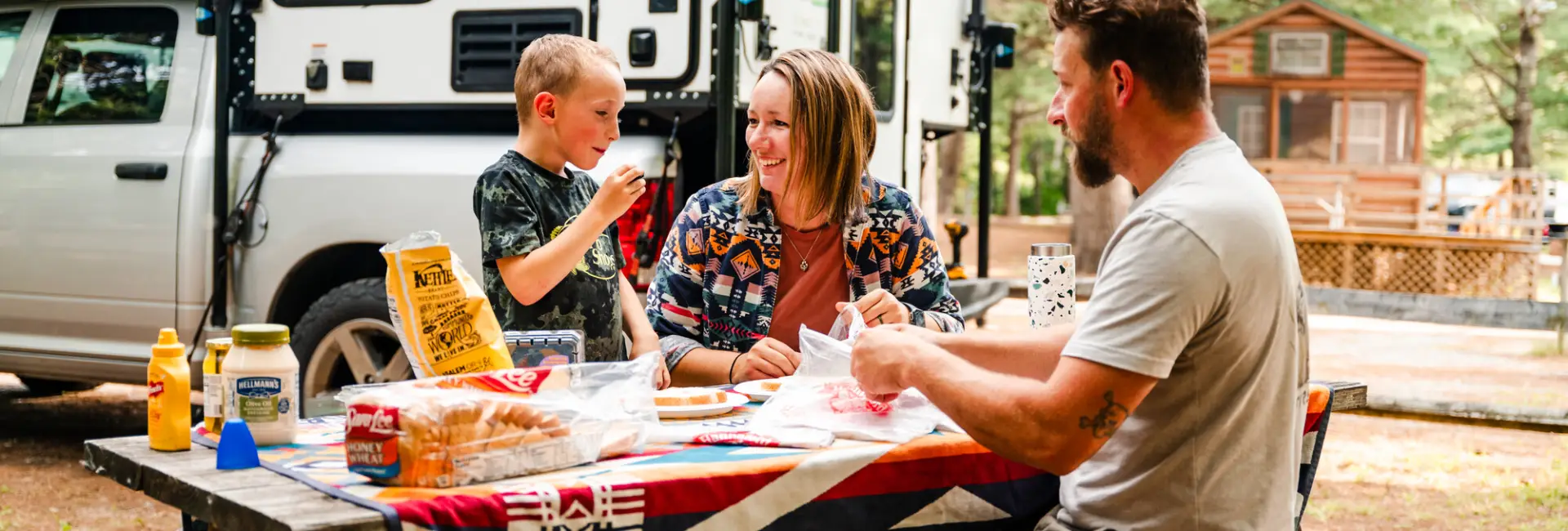 A family of three make sandwiches at a campsite. 