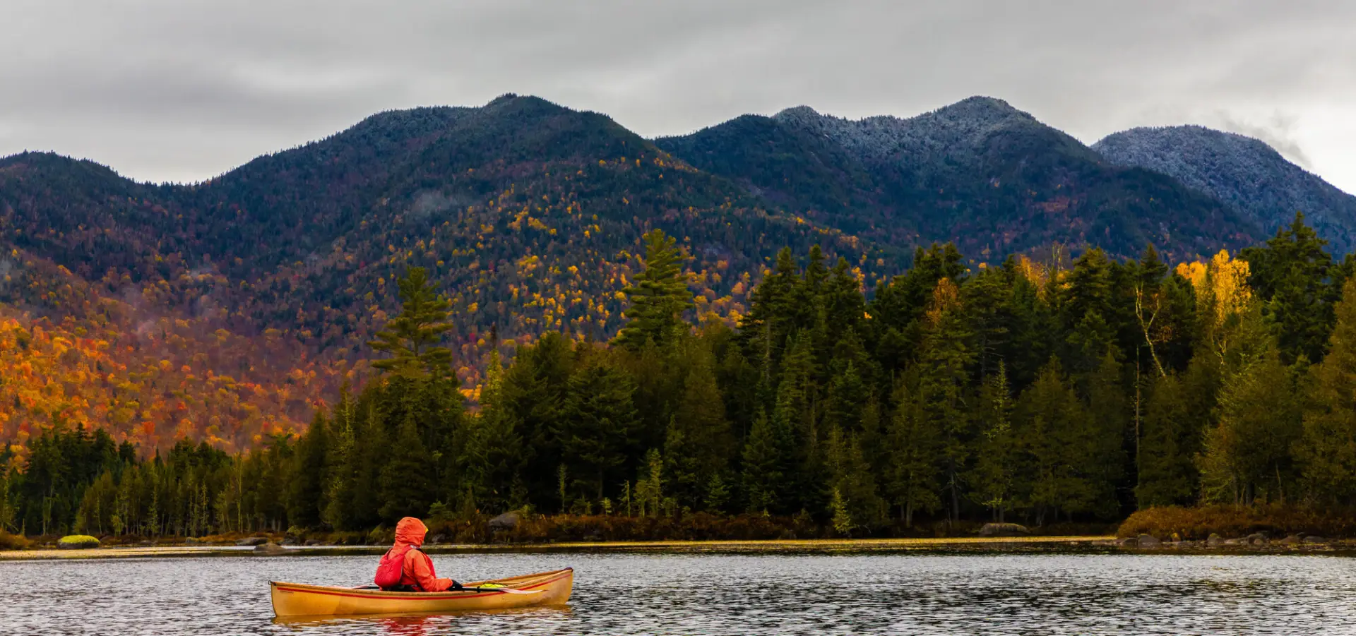 A man canoes on a lake in fall with mountains in the background.