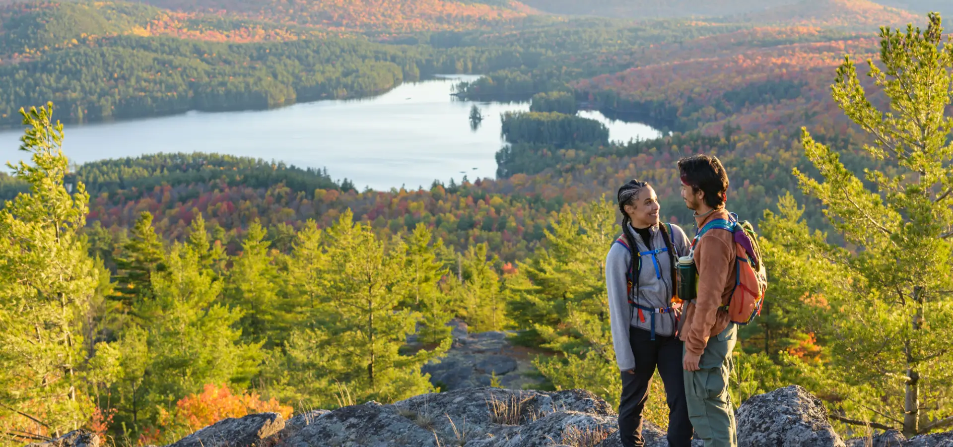 A man and woman stand on top of a mountain in fall. 