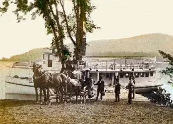 Horse and carriage with some smartly dressed men stand in front of a large boat in this historical photo.