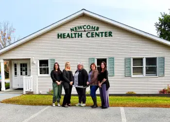 Five smiling women stand out side of the Newcomb Health Center building