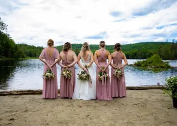 Bridal party stands in the sand by the water holding bouquets behind their backs., A bride and groom on the bridge share a kiss., Logo for Morningside Adirondacks.