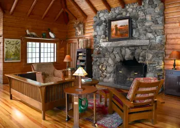 A huge stacked stone fireplace flanked with leather chairs in a wooden walled room with tall exposed rafter ceilings.