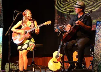 Two people sit on stage playing guitar on a colorful stage