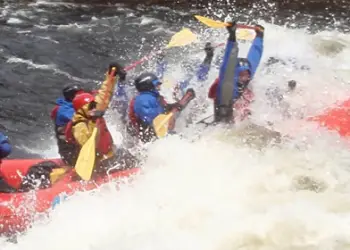 Paddles up overhead while hitting the white water, Inflatable rafts on the edge of the river with tents in the background
