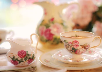 A porcelain tea set with a dark pink rose motif sits on linen table cloth covered surface