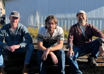 Three men sit on railroad ties by the train tracks.