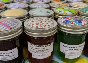 Many jars of jam sitting in clean lines with colorful fabric covering the lids