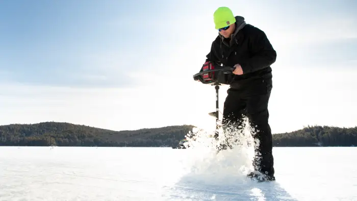 Man using an ice auger on a frozen lake.