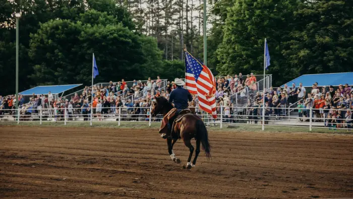 A man carrying an American Flag rides a horse down the fairway while spectators look on.