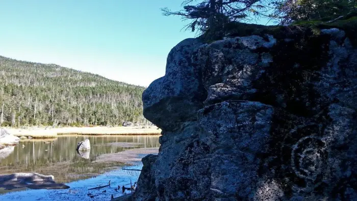 A view of an interesting rock formation in front of a small mountain pond.