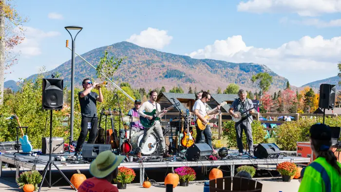 Band plays live music on stage decorated with pumpkins and mums with mountain in background