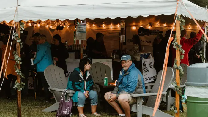 Spectators sit in Adirondack chairs under tent