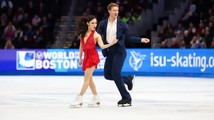  wave to crowds from on the ice while young girls in blue dresses skate behind