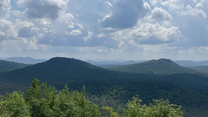Hikers sit and stand on rocky summit of Goodman Mountain looking at and photographing the view.