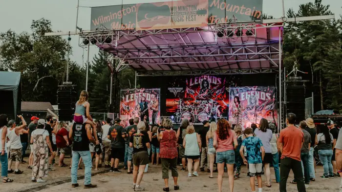 Crowd of people stands looking at music festival stage outdoors in summer