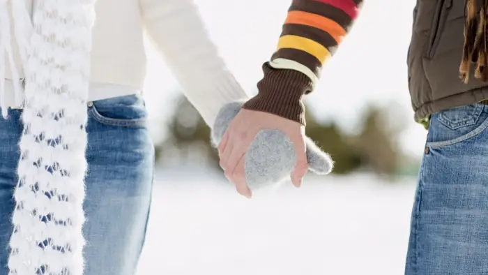 Two people holding gloved hands and walking in the snow