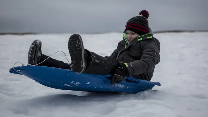 A kid on sled going down a wintry slope
