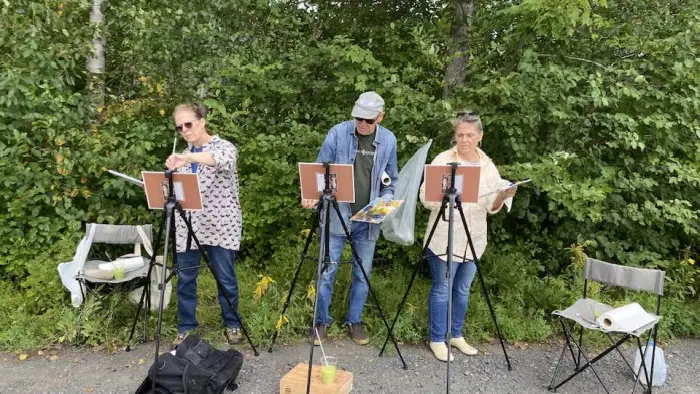 Three people standing at their easles painting the natural scene before them