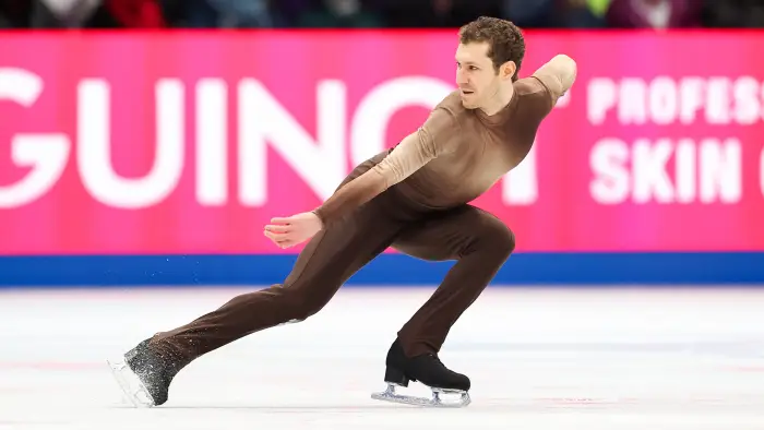 Male figure skater holds up female figure skater while performing on ice with a large crowd watching