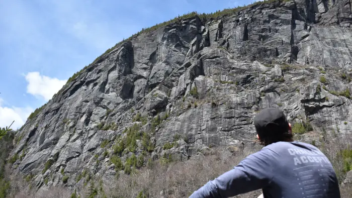 A hiker looks up at a large cliff face