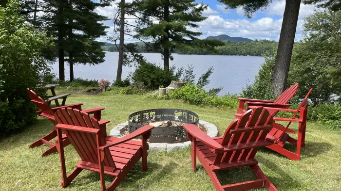 Adirondack Chairs circling a fire pit overlooking the lake through the trees