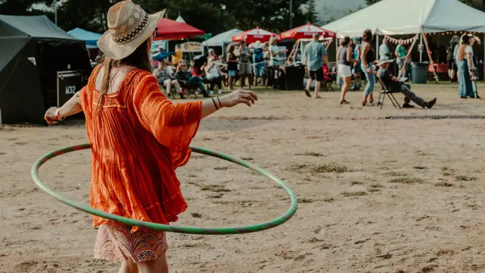 Woman in red dress and straw hat hula hoops in front of smallfestival crowd