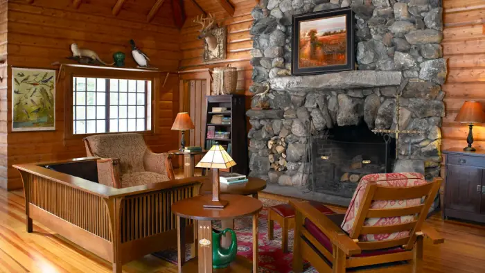 A huge stacked stone fireplace flanked with leather chairs in a wooden walled room with tall exposed rafter ceilings.