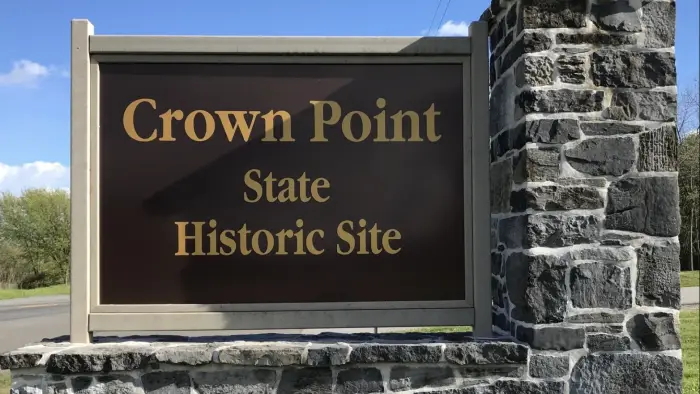 A large brown sign on a stacked stone post reading Crown Point Historic Site in gold letters