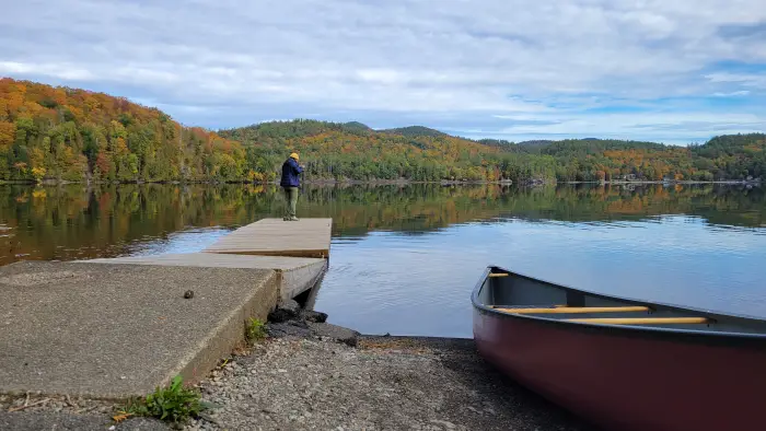 A canoe next to a dock with a person taking in a fall view