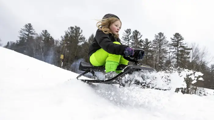 A young kind heading down a hill on a snow sled