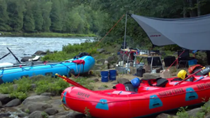 Inflatable rafts on the edge of the river with tents in the background