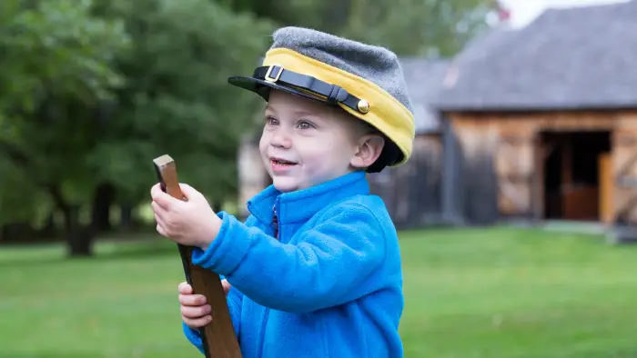 A small boy holding a wooden gun wearing a Confederate soldier's cap