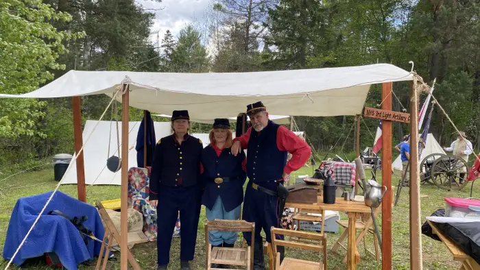 several people dressede in the civil war era standing under a canvas tent