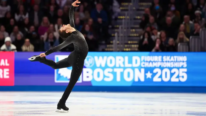 Female figure skater in a red dress and male figure skater in a blue suit perform side by side on ice