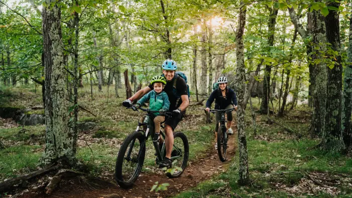 Family riding through the woods&#44; with a little one strapped to a parent.