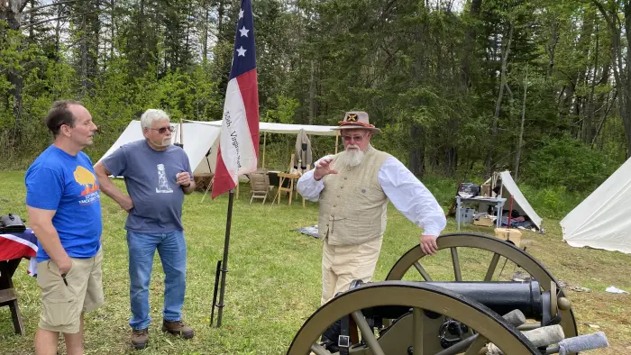 A man in period dress talking with two other men about a civil war canon