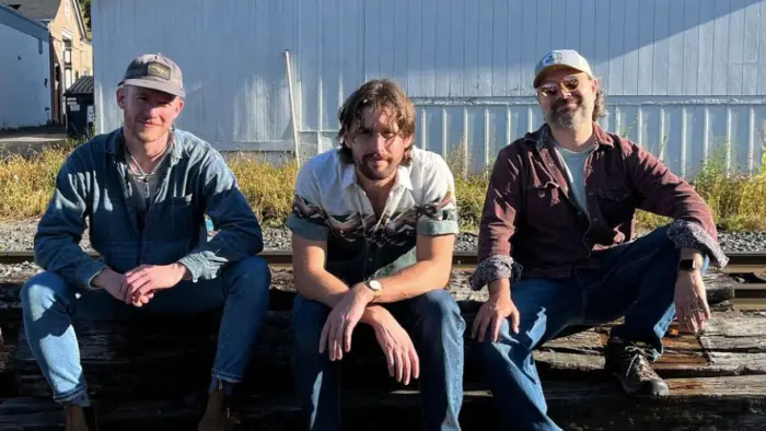 Three men sit on railroad ties by the train tracks.